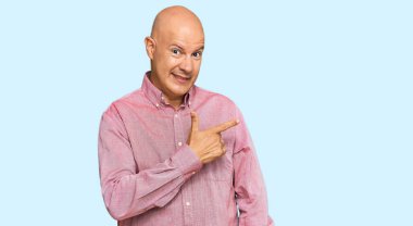 Orta yaşlı, kel, günlük kıyafetler giyen, neşeli, yüzünde mutlu ve doğal bir ifadeyle elleri ve parmaklarıyla yüzünü gösteren bir gülümseme olan bir adam. 