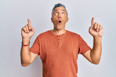 Yakışıklı, orta yaşlı, rahat kıyafetler giyen, şaşırmış ve şaşırmış, parmaklarıyla işaret eden ve kollarını kaldıran olgun bir adam.. 