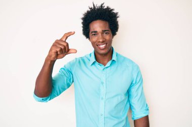 Afro saçlı, sıradan giyinmiş, gülümseyen, kendine güvenen, el hareketleriyle küçük boy işareti yapan, parmakları ve kamerası olan yakışıklı Afro-Amerikan bir adam. ölçüm kavramı. 