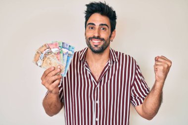 Sakallı yakışıklı İspanyol adam Kanada doları tutuyor gururla bağırıyor, zaferi ve başarıyı kutluyor. 