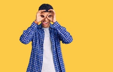 Genç Afrikalı Amerikalı sıradan kıyafetler giymiş dürbün gibi jest yapıyor, gözleri parmaklarından bakıyor. çılgın ifade. 