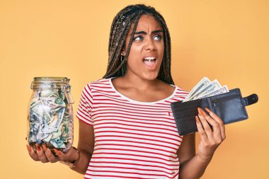 Tasarruf kavanozu ve cüzdanı olan, öfkeli ve öfkeli bağıran öfkeli, öfkeli ve öfkeli, saçları örgülü genç Afro-Amerikalı bir kadın. öfke ve agresif konsept. 