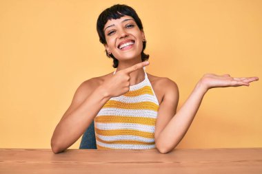 Masanın üzerinde oturan güzel esmer kadın hayrete düşmüş ve kameraya gülümsüyordu. Elle ve parmakla gösteriyordu.. 