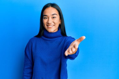 Genç Asyalı kadın, günlük kışlık süveter giyiyor. Gülümsüyor. Avuç içi dolusu yardım ve kabullenme sunuyor.. 