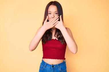 Yazlık giysiler giyen genç güzel Çinli kız yanlışlıkla elleriyle ağzını kapatırken şok oldu. gizli kavram. 