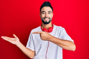 Sakallı genç adam kulaklık takarak müzik dinliyor kameraya hayret ediyor ve gülümsüyor.. 