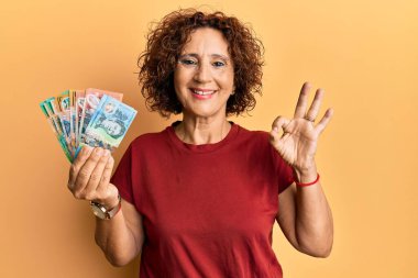 Güzel, orta yaşlı, elinde Avustralya doları olan olgun bir kadın parmaklarıyla imza atıyor, gülümseyerek mükemmel bir sembol oluşturuyor. 