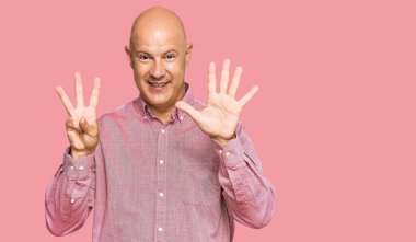 Orta yaşlı, kel, günlük kıyafetler giyen, 8 numaralı parmaklarıyla işaret eden, kendinden emin ve mutlu gülümseyen bir adam.. 