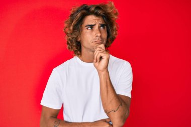Latin asıllı genç bir adam, günlük beyaz tişört giyiyor ciddi bir yüz ifadesi, eli çenesinde soru sormayı düşünüyor, kafa karıştırıcı bir fikir. 