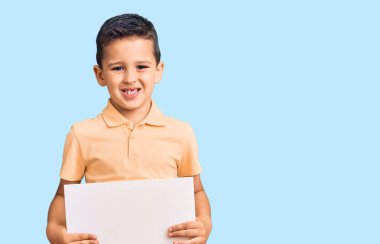 Elinde boş yeri olan karton bir afiş tutan sevimli bir çocuk. Olumlu ve mutlu görünüyor. Kendine güvenen bir gülümsemeyle dişlerini gösteriyor. 