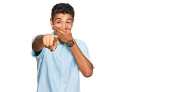 Genç, yakışıklı, Afro-Amerikan bir adam. Günlük kıyafetler giyip sana gülüyor. Eli ağzında kamerayı işaret ediyor. 