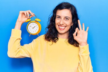 Güzel İspanyol bir kadın çalar saati tutuyor. Parmaklarıyla imza atıyor, gülümsüyor. Mükemmel bir sembol. 