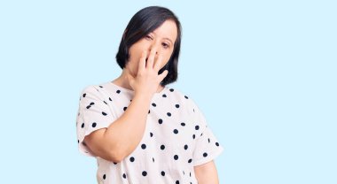 Down sendromlu esmer kadın gündelik kıyafetler giyiyor. Ağzı eliyle kapatmaktan sıkılmış. Huzursuz ve uykulu.. 