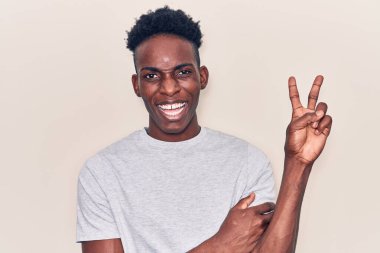 Genç Afro-Amerikalı sıradan kıyafetler giyen, gülen yüzlü, kameraya göz kırpan zafer işareti yapan genç bir adam. İki numara.. 