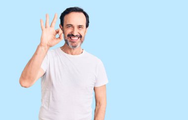 Orta yaşlı yakışıklı bir adam günlük tişört giyiyor, gülümsüyor ve el ve parmaklarıyla 