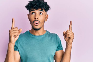 Gündelik giysiler giyen genç Arap yakışıklı adam şaşırmış ve şaşırmış bir şekilde yukarı baktı ve parmaklarıyla işaret etti ve kollarını kaldırdı.. 