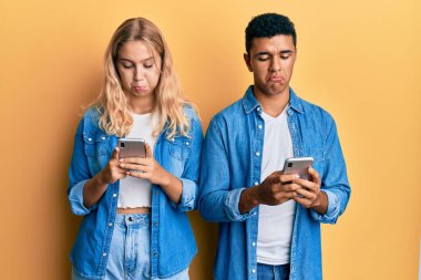 Akıllı telefon kullanan ırklar arası genç bir çift sıkıntılı ve endişeli, kızgın ve korkmuş bir şekilde ağlıyorlar. hüzünlü ifade. 
