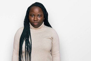 Saçları örgülü genç siyahi bir kadın. Yüzünde ciddi bir ifade olan sıradan bir kazak giyiyor. Basit ve doğal bir şekilde kameraya bakıyorsun.. 