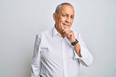 Yakışıklı, beyaz gömlek giyen, kameraya kendinden emin, kollarını kavuşturmuş ve çenesini kaldırmış gülümseyen bir adam. Olumlu düşünmek. 