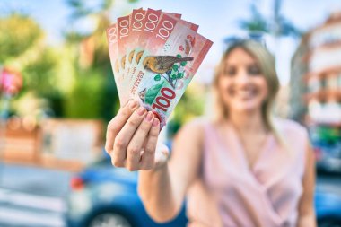 Genç sarışın kadın gülümsüyor. Yeni Zelanda 'yı mutlu ediyor. Şehirde 100 dolarlık banknotlar tutuyor..