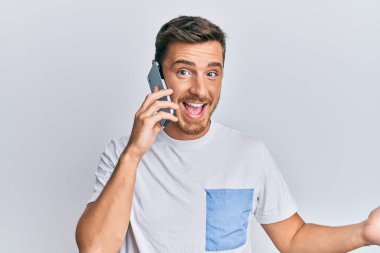 Yakışıklı beyaz adam akıllı telefonda konuşuyor başarıyı mutlu bir gülümsemeyle kutluyor ve kazanan el kaldırarak ifade ediyor. 