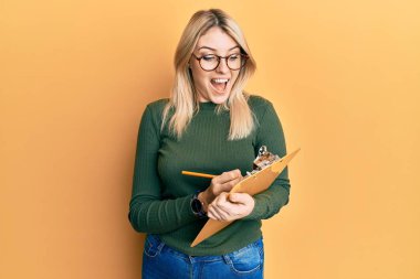 Kafkasyalı genç bir kadın kontrol listesi panosuna yazı yazıyor. Çılgınlığı kutluyor ve başarıya hayret ediyor. Gözleri açık, heyecanlı bir şekilde bağırıyor.. 