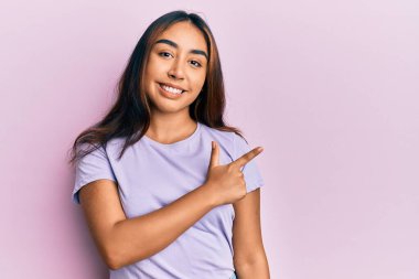 Genç Latin kadın gündelik giysiler giyiyor. Gülümsüyor, elleri ve parmakları yana doğru işaret ediyor. 