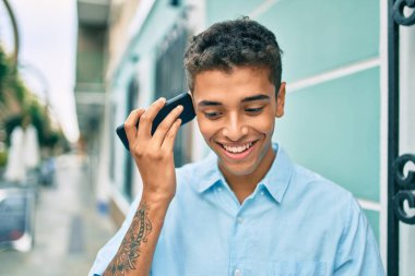 Genç Latin adam gülümsüyor. Şehirde akıllı telefon kullanarak mutlu bir sesli mesaj dinliyor..