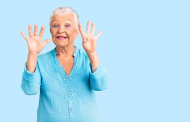 Mavi gözlü, gri saçlı, yaz elbisesi giyen, dokuz numaralı parmaklarıyla işaret eden, kendinden emin ve mutlu gülümseyen son sınıf güzeli kadın.. 