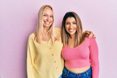 Mutlu ve havalı bir gülümsemeyle pembe arka planda yan yana duran iki arkadaş. şanslı kişi. 