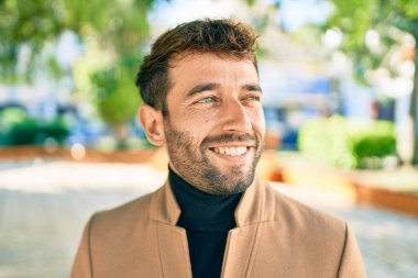 Zarif ceket giyen yakışıklı iş adamı dışarıda mutlu bir şekilde gülümsüyor.