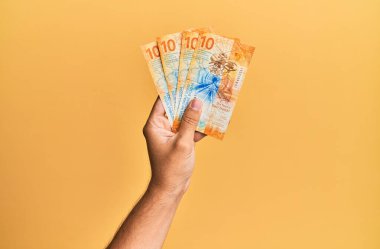 Issız sarı arka planda İsviçre 10 franklık banknotlar tutan İspanyol bir adam..