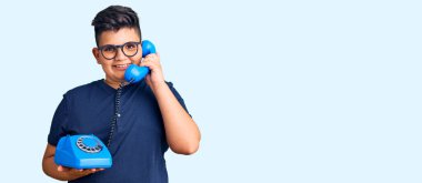 Kaliteli telefon kullanan küçük çocuk pozitif ve mutlu görünüyor. Kendine güvenen bir gülümsemeyle ayakta duruyor ve dişlerini gösteriyor. 