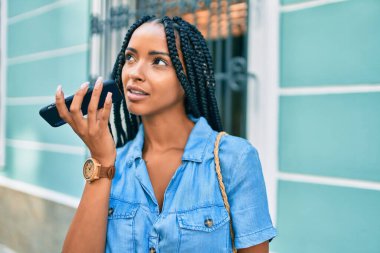 Genç Afrikalı Amerikalı kadın gülümsüyor. Şehirdeki akıllı telefondan sesli mesaj gönderiyor..