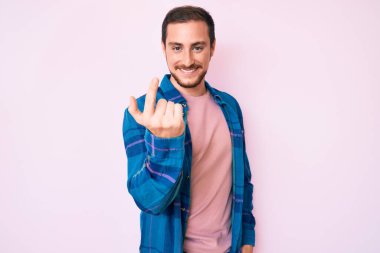 Gündelik kıyafetler giyen genç yakışıklı adam seni buraya çağırıyor. El kol hareketi yap. Mutlu bir şekilde karşıla ve gülümse. 