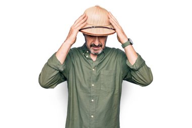 Tatilde olan orta yaşlı bir turist izole edilmiş beyaz bir arka planı olan kaşif şapkası takıyor ve başı ağrıyor çünkü stres altında. Migren ağrısı..