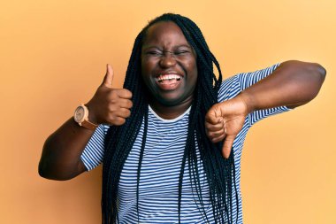 Örgülü genç siyahi kadın baş parmağını kaldırıyor ve baş parmağını kaldırıyor. Gülümsüyor ve kahkahalarla gülüyor. Çünkü komik, çılgınca bir şaka.. 