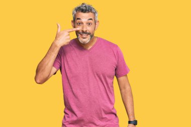 Orta yaşlı, gri saçlı, günlük giysiler giyen, el parmağı ve burunla işaret eden, neşeli gülümseyen bir adam. güzellik konsepti 