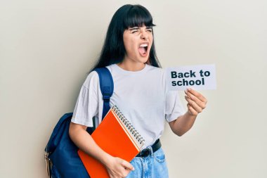 Sırt çantası takan genç İspanyol kız okul afişini geri tutuyor kızgın ve öfkeli çığlıklar atıyor, öfkeyle bağırıyor. öfke ve agresif konsept. 