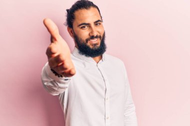 Gündelik kıyafetler giyen genç bir Arap dostça bir selamlama ve hoş geldin hediyesi olarak el sıkışmayı sunuyor. başarılı iş. 