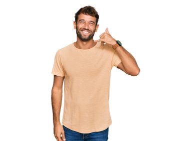 Sakallı, sıradan tişörtler giyen, el ve parmaklarıyla telefon hareketi yapan telefonda konuşan yakışıklı bir genç. iletişim kavramları. 