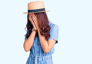 Genç, güzel Çinli kız, yaz şapkası takıyor ve ağlarken suratını ellerle kapatıyor. depresyon kavramı. 