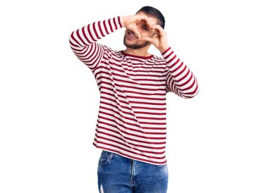 Çizgili kazak giyen, eli ve parmaklarıyla kalp şekli yapan genç yakışıklı adam tabeladan bakıp gülümsüyor. 