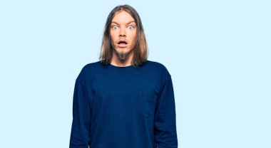 Uzun saçlı, beyaz, sıradan bir süveter giyen yakışıklı, şaşkınlık ve şaşkınlık içinde bir ifade, korku ve heyecan dolu bir yüz.. 