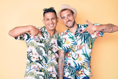 Yaz şapkası ve Hawaii tişörtü giyen, kendine güvenen, gülümseyen, kendini gururlu ve mutlu gösteren iki genç gay.. 