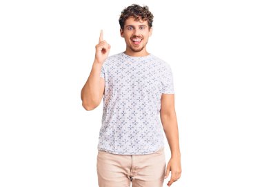 Kıvırcık saçlı, sıradan giyinen genç ve yakışıklı bir adam başarılı bir fikri işaret ediyor. Heyecanlı ve mutlu. Bir numara.. 