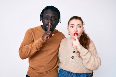 Sıradan kıyafetler giyen ırklar arası bir çift parmakları dudaklarında sessiz olmak istiyorlar. sessizlik ve gizli konsept. 