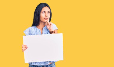 Genç, güzel, boş afiş taşıyan Latin bir kız. Ciddi bir yüzü var. Soru sormayı düşünüyor. 