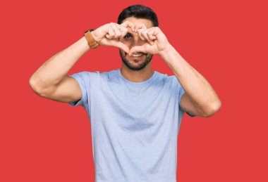 Gündelik giysiler giymiş, elleri ve parmaklarıyla kalp şeklinde gülümseyen genç İspanyol adam tabeladan bakıyor. 