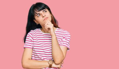 Elleri çenesinde gündelik giysiler içinde soru soran genç İspanyol kız, düşünceli ifade. Düşünceli bir yüzle gülümsüyor. şüphe kavramı. 